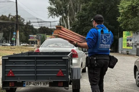 Волонтер місії Проліска несе дерев’яні дошки до причепа