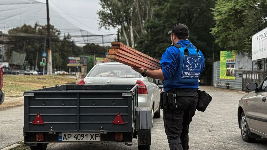 Волонтер місії Проліска несе дерев’яні дошки до причепа