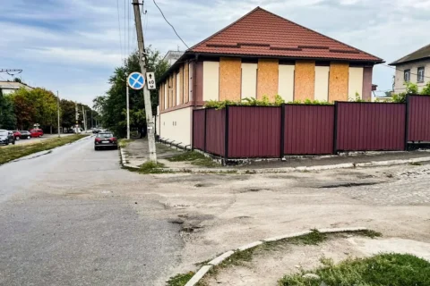 Міське перехрестя з будинком із забитими вікнами та бордовим парканом