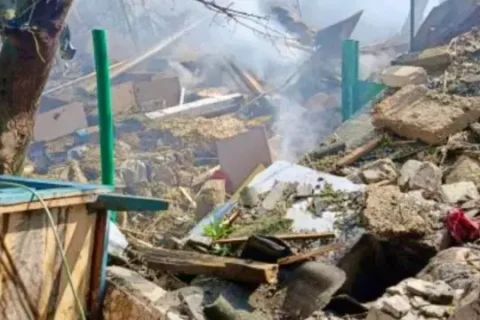 Зруйнований цегляний будинок із вибитими вікнами та люди біля нього