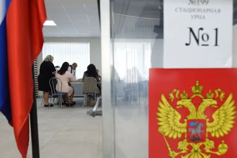Російський прапор і герб на скляній кабінці стаціонарної урни, люди за столом