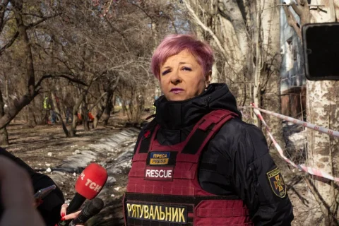 Жінка-рятувальник у червоному жилеті дає інтервю журналістові з мікрофоном